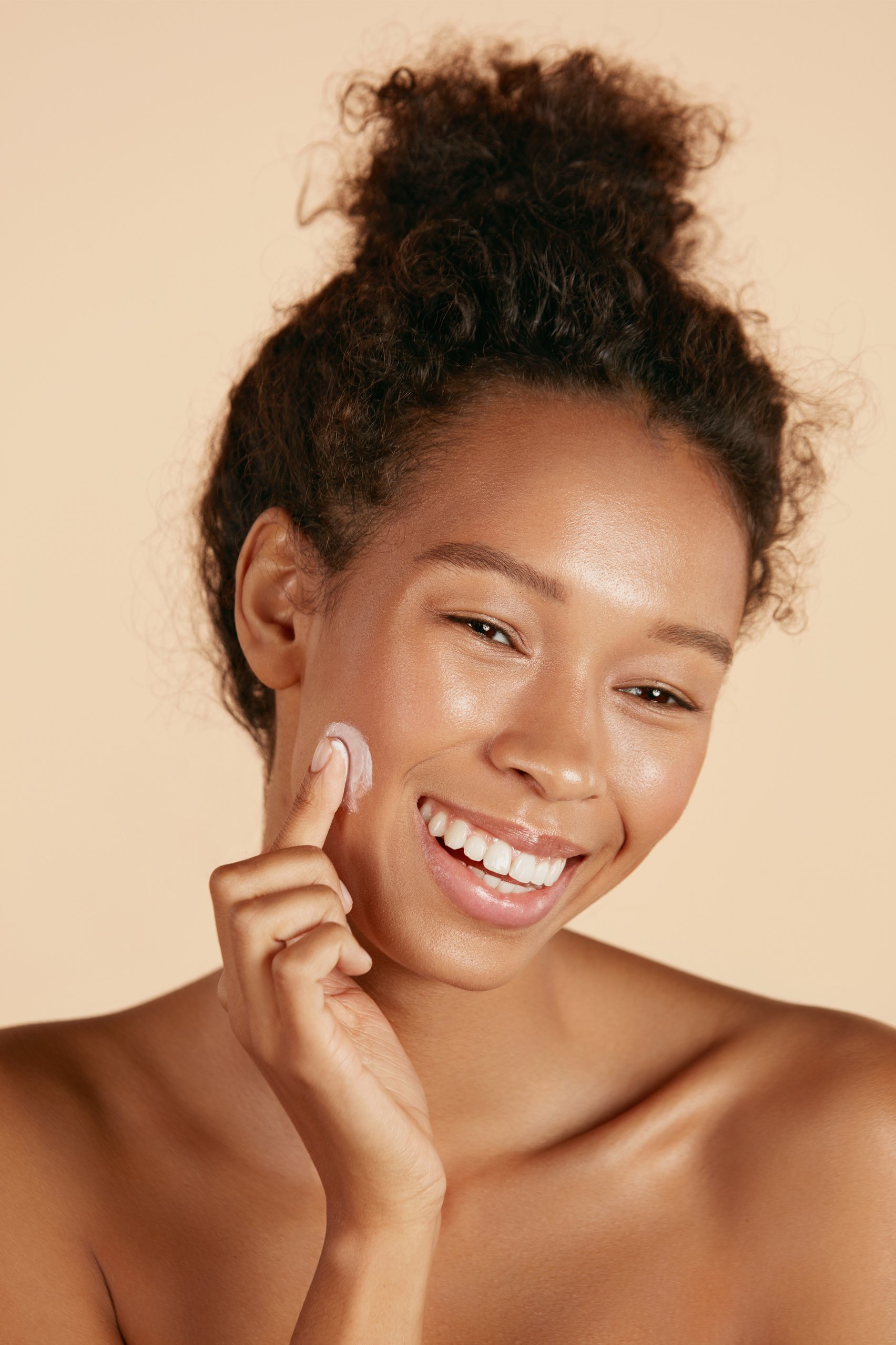 Face skin care. Woman applying cosmetic cream on skin portrait