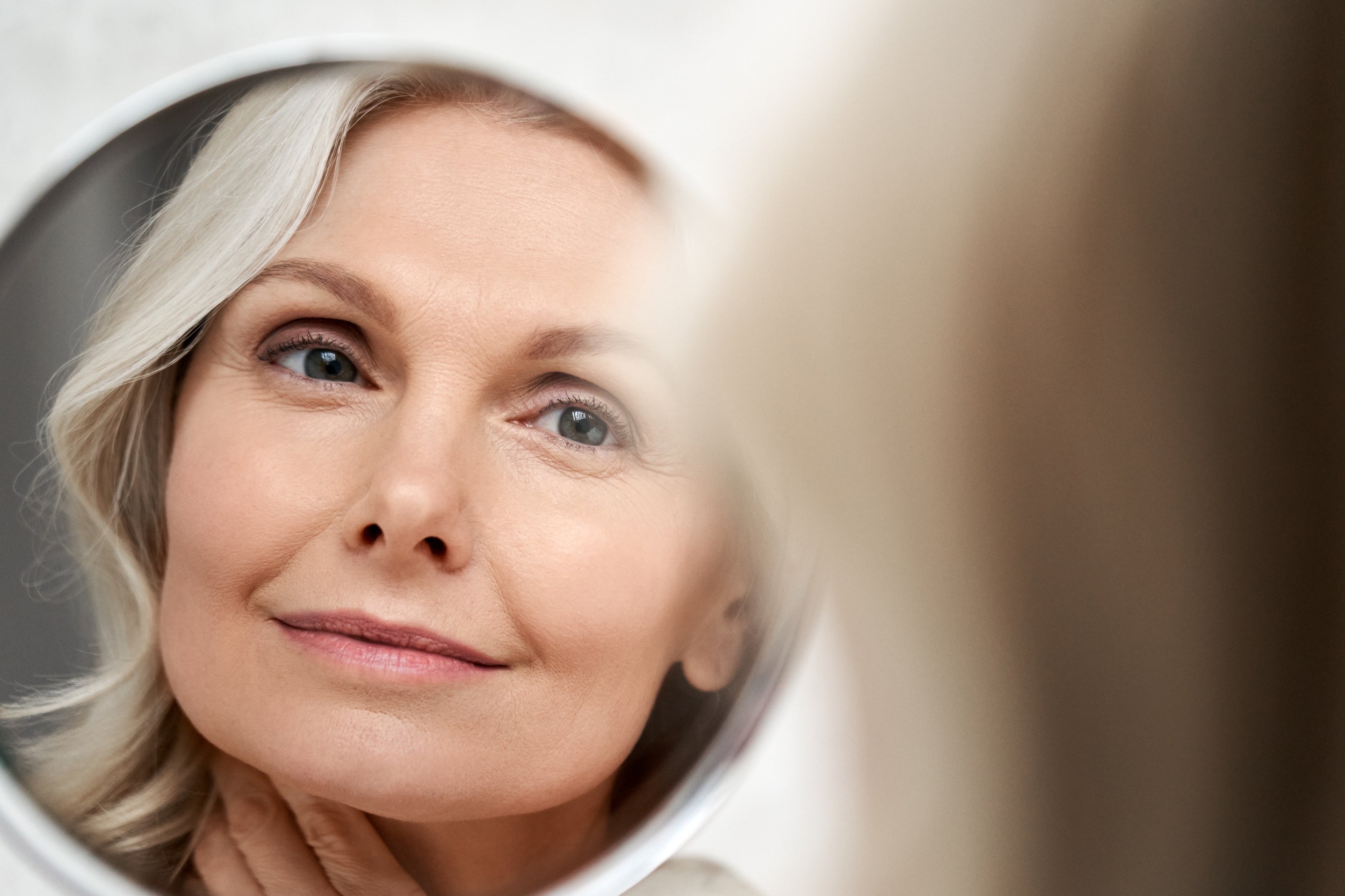 Happy 50S Middle Aged Woman Touching Face Skin Looking in Mirror Reflection.